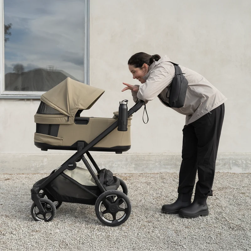 Förälder lutar sig över Thule Charm 2 in 1 utomhus – kombivagn att hyra hos Parently