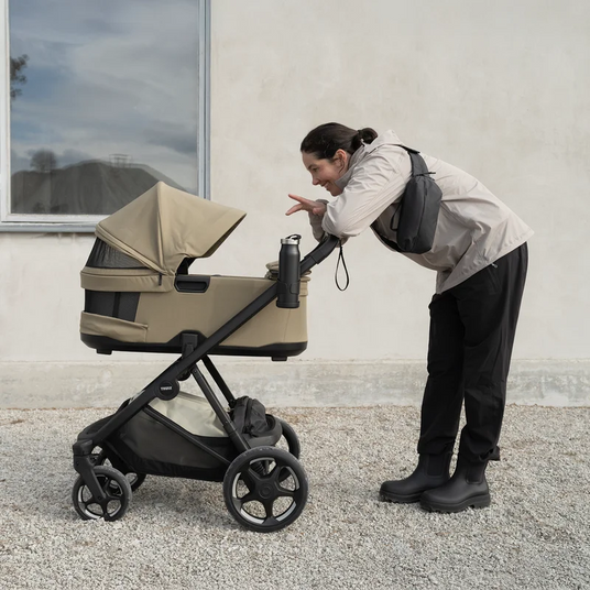 Förälder lutar sig över Thule Charm 2 in 1 utomhus – kombivagn att hyra hos Parently