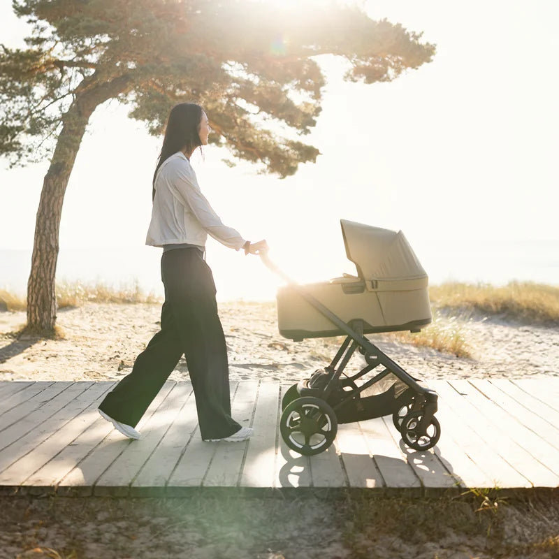 Mamma promenerar med hyrd Thule Charm 2 in 1 barnvagn längs en solig strandpromenad
