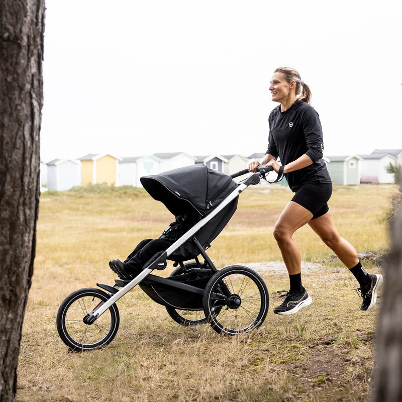 Förälder springer med Thule Glide 3 på gräs och grus, hyrd joggingvagn från Parently