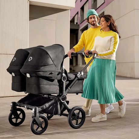 Par på promenad med barnevognen Bugaboo Donkey 5 Twin til tvillingar i sort med två liftar