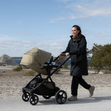 Förälder promenerar med Thule Charm 2 in 1 vid vattnet – hyr barnvagn hos Parently
