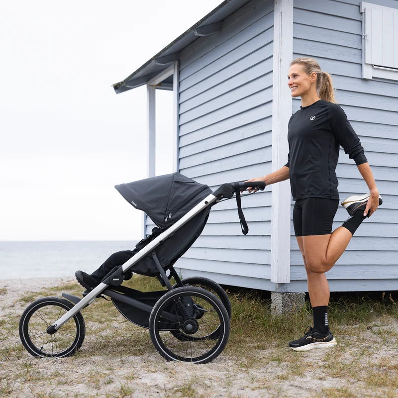 Förälder sträcker ut bredvid Thule Glide 3 joggingvagn under en paus, att hyra hos Parently