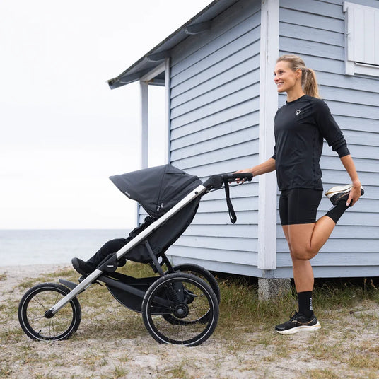 Förälder sträcker ut bredvid Thule Glide 3 joggingvagn under en paus, att hyra hos Parently